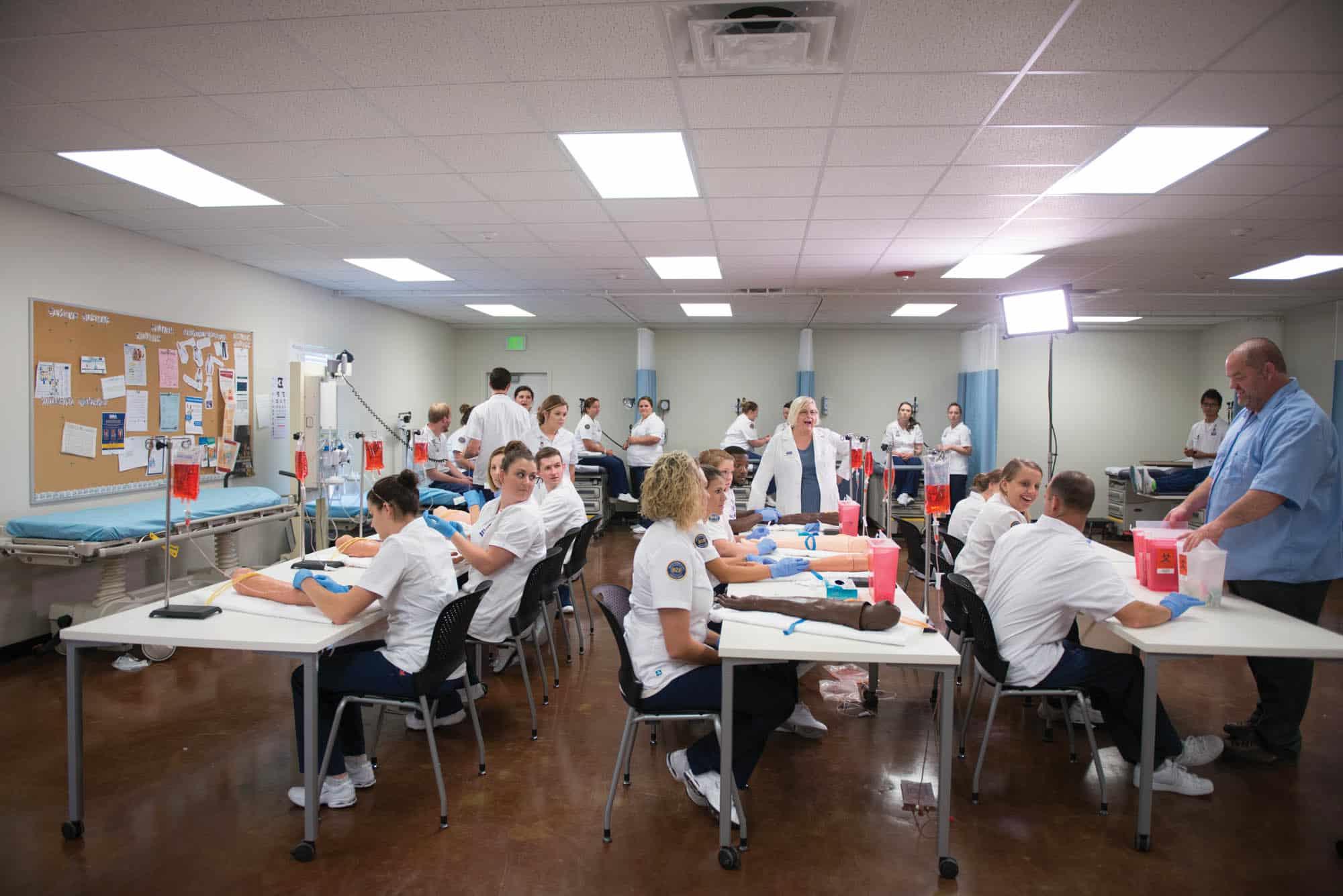 A group of nursing student in a classroom. It appears they are learning to draw out blood from an arm.