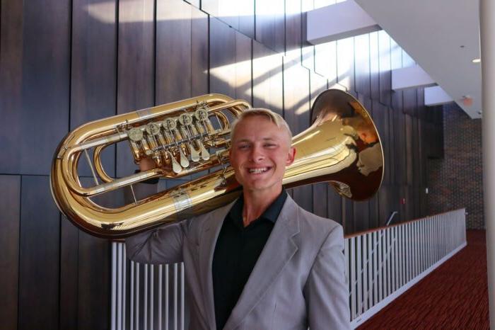 A person posing for a photo while holding a Euphonium.